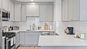 Uma cozinha moderna com armários cinzas, fogão de aço inoxidável, micro-ondas, torradeira e máquina de café.