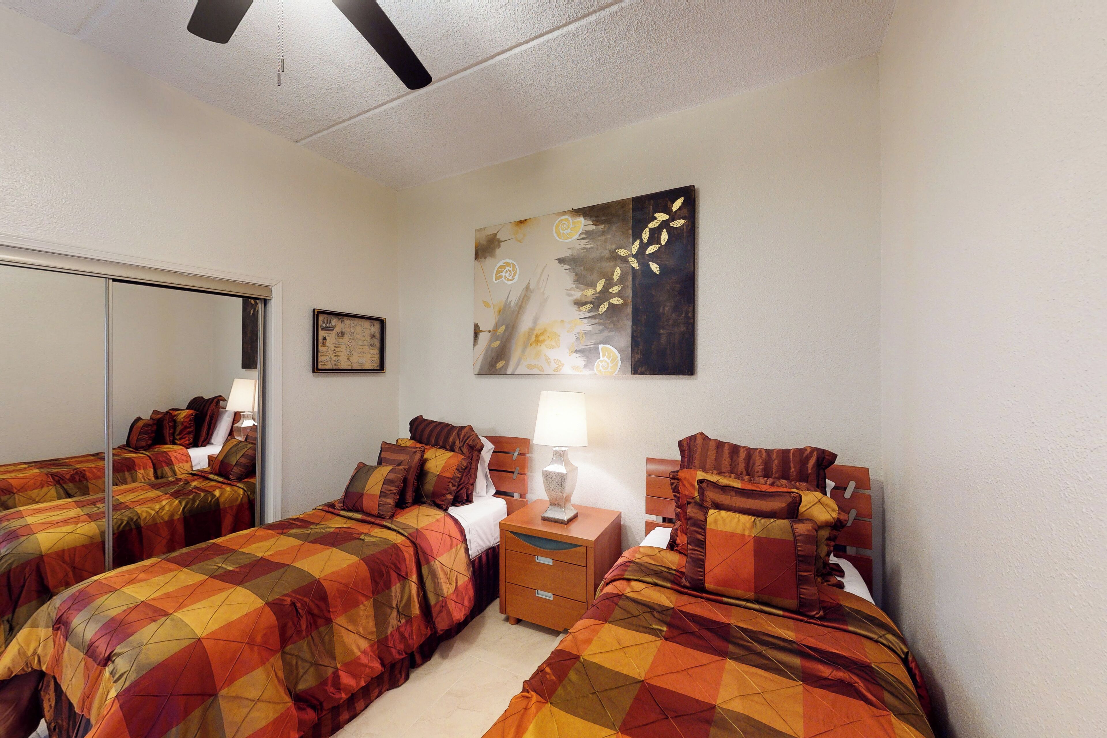 A hotel room with two beds, a nightstand, a lamp, a painting, and a mirror.