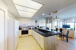 A modern kitchen with a central island, white cabinetry, and a dining area with a sofa and chairs. - Gulf-View 3BR, Patio, Yard: Suntide III - Unit 101 (South Padre Island)
