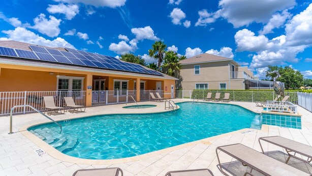 A swimming pool with lounge chairs, a building with solar panels, and a clear blue sky. - 17517 Dream (Clermont)