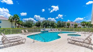 Un área de piscina con varias piscinas, sillones de descanso y un cielo azul despejado.