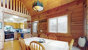 A wooden cabin interior with a dining area, kitchen, and a staircase leading to an upper level. - Steps to Three Bears Resort! Outdoorsy Escape (Warrens)