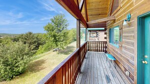 A wooden cabin with a balcony overlooking a grassy area and trees. - Steps to Three Bears Resort! Outdoorsy Escape (Warrens)
