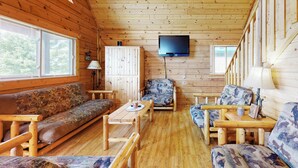 A wooden cabin interior with a sofa, armchairs, a table, and a television mounted on the wall. - Steps to Three Bears Resort! Outdoorsy Escape (Warrens)