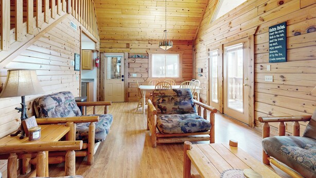 A wooden cabin interior with a dining area, two sofas with patterned cushions, a wooden staircase, and a chandelier. - Steps to Three Bears Resort! Outdoorsy Escape (Warrens)