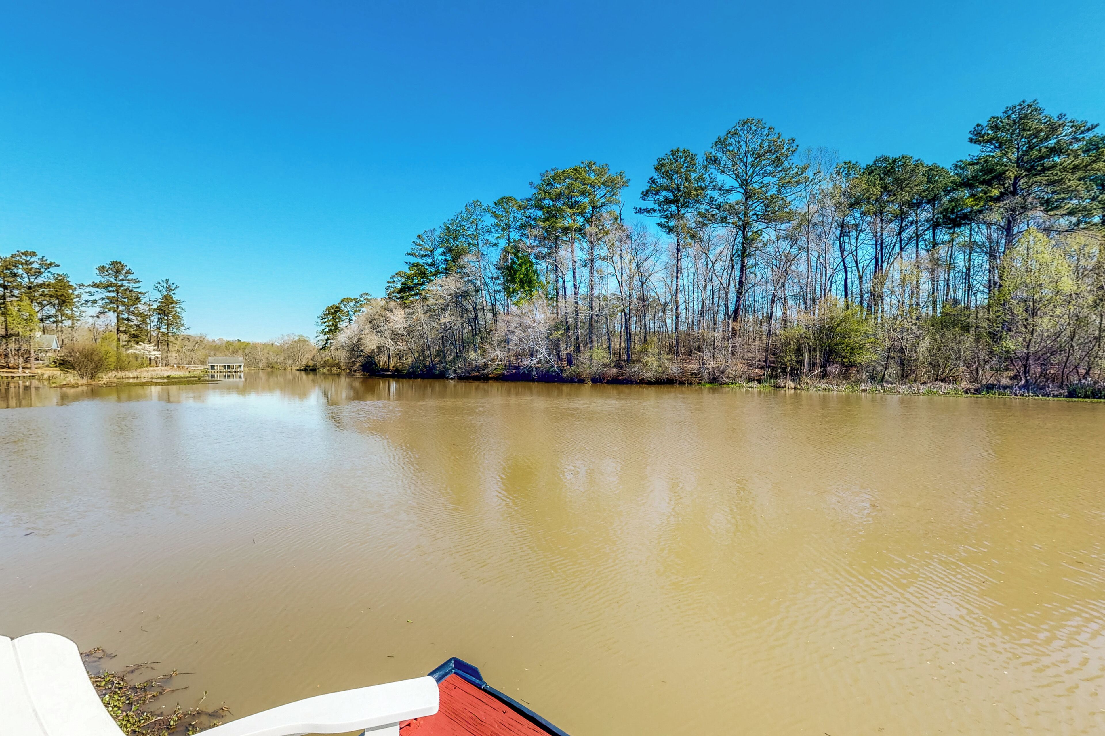 A calm river with trees on the banks and a small building in the distance.