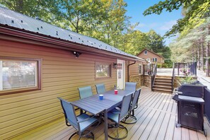 En træterrasse med et bord og stole, grill og et overdækket område med trapper til en hytte.