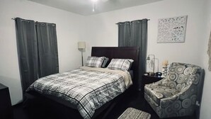 Ein Schlafzimmer mit einem Bett, einem Sessel, einem Nachttisch, einer Lampe und einem Deckenventilator.