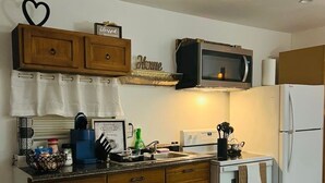 Eine kompakte Küche mit Holzausstattung, einer Mikrowelle, einem Kühlschrank und einem Herd.