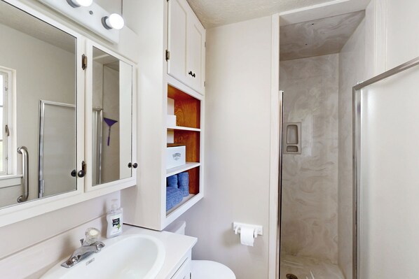 A bathroom with a white sink, mirror, and cabinets. There is a shower area with a glass door. - Farmington Family Home w/ Private Patio (Farmington)