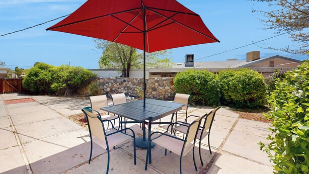 Eine Außenpatio mit Tisch und Stühlen, einem roten Sonnenschirm und einer Steinsäule im Hintergrund.
