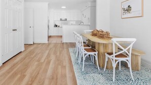 Une cuisine moderne avec des meubles blancs, une table à manger en bois avec des chaises blanches et un tapis à motifs bleus.