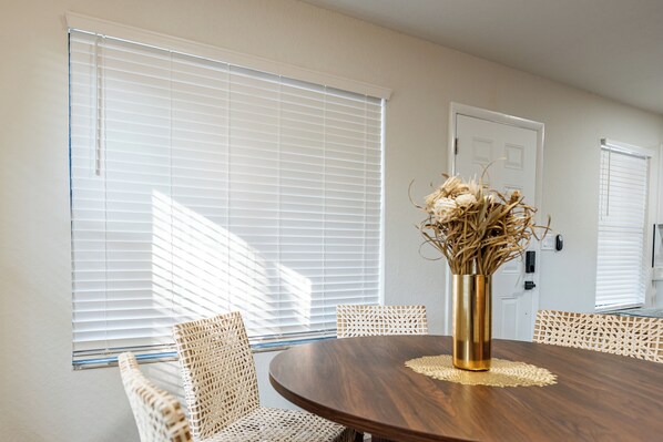 A dining area with a round wooden table, four wicker chairs, and a vase with dried plants.