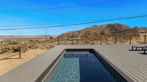 Ein rechteckiger Pool mit Holzterrasse, umgeben von einer Wüstenlandschaft mit Bergen im Hintergrund.