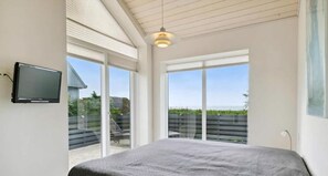 A bedroom with a bed, a TV, large sliding glass doors, and a ceiling light. - Bright and lovely seaside holiday home (Ebeltoft)