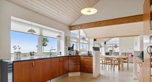 A modern kitchen with wooden cabinets, a central island, and large windows offering a view. - Bright and lovely seaside holiday home (Ebeltoft)