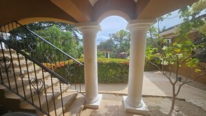 A covered outdoor staircase with white columns, leading to a garden area with a small tree and a hedge. - Main floor, Family unit, 3 bed, fresh, clean, inside Tamarindo w incredible pool (Tamarindo)