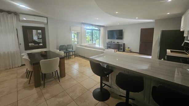 A modern kitchen with a large island, dining area with chairs, and a TV mounted on the wall. - Main floor, Family unit, 3 bed, fresh, clean, inside Tamarindo w incredible pool (Tamarindo)