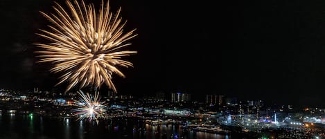 A nighttime cityscape with a large firework display over a body of water, reflecting city lights.