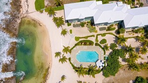 Luftaufnahme eines Resorts mit Schwimmbad, Strand und Palmen.