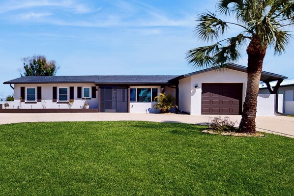 A modern two-story house with a garage, a well-maintained lawn, and a palm tree. - Golf Cart & Heated Pool: Rotonda West Getaway! (Rotonda West)