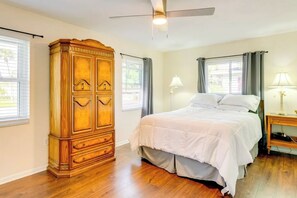 A bedroom with a wooden armoire, a bed with white bedding, two bedside lamps, and a ceiling fan. - Golf Cart & Heated Pool: Rotonda West Getaway! (Rotonda West)