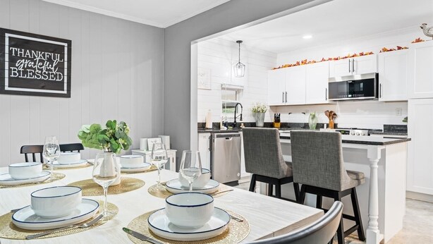 A dining area with a table set for four, a kitchen in the background, and a sign on the wall. - KnoxHaven | 5 Min UT•Hot Tub•Firepit•Theater•Games (Knoxville)