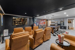 A room with a pool table, leather chairs, a large painting, and a popcorn machine. - KnoxHaven | 5 Min UT•Hot Tub•Firepit•Theater•Games (Knoxville)