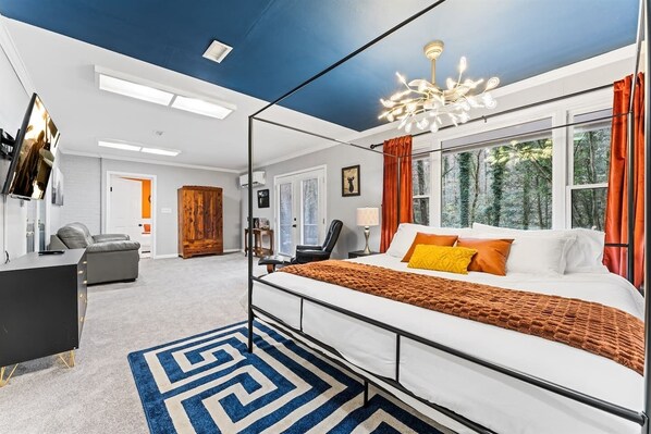 A modern bedroom with a bed, a desk, a chair, and a large window with curtains. - KnoxHaven | 5 Min UT•Hot Tub•Firepit•Theater•Games (Knoxville)