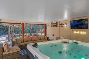 Boblebad med udsigt til træer, en sofa og et fjernsyn ophængt på væggen.