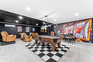 A pool table with surrounding leather chairs, a checkered floor, and a slot machine mural. - KnoxHaven | 5 Min UT•Hot Tub•Firepit•Theater•Games (Knoxville)