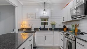 A modern kitchen with white cabinetry, granite countertops, stainless steel appliances, and a farmhouse-style window. - KnoxHaven | 5 Min UT•Hot Tub•Firepit•Theater•Games (Knoxville)