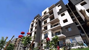 A multi-story residential building with balconies, a clear sky, and some greenery. - Elegant Apartment at Sheikh Zayed Compound (Sheikh Zayed City)