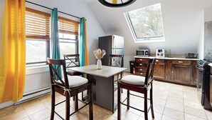 A kitchen with a dining area, wooden cabinets, a refrigerator, a microwave, and a window with blinds.