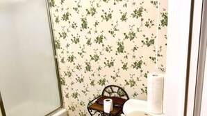 Ein Badezimmer mit Toilette, einem kleinen Tisch mit Toilettenpapier und einer Duschkabine.
