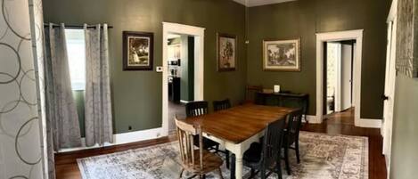 Un coin repas avec une table et des chaises en bois, un tapis à motifs et des murs verts.