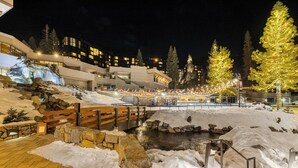 A snow-covered outdoor area with a wooden bridge, stone walls, and a water feature.