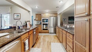 A modern kitchen with wooden cabinets, stainless steel appliances, granite countertops, and a large island with a sink.