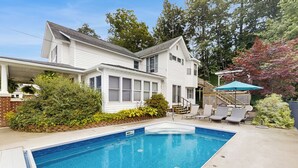 A two-story house with a swimming pool, a covered patio, and a deck with outdoor furniture.