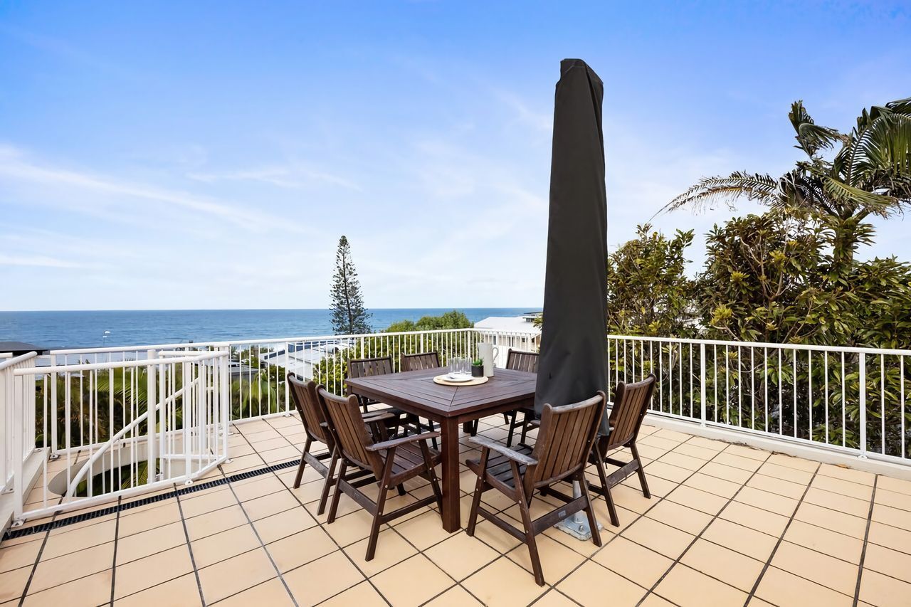 Eine Außenpatio mit Tisch und Stühlen, einem hohen Sonnenschirm und Blick auf das Meer.