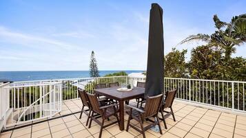 Eine Außenpatio mit Tisch und Stühlen, einem hohen Sonnenschirm und Blick auf das Meer.