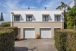 A modern two-story building with a flat roof, three windows with shutters, and two garage doors.