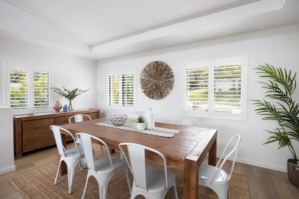 A dining area with a wooden table, white chairs, and a decorative wall piece.