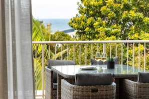 A balcony with wicker furniture, a glass table, and two wine glasses.