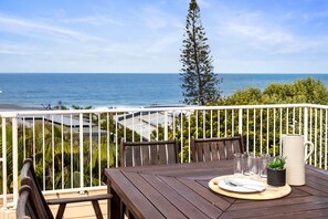 A wooden table with a view of the ocean, a potted plant, and a pitcher on a balcony.