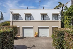 A modern two-story building with a flat roof, three windows on the upper floor, and two garage doors on the lower floor. - Breezy Beach Haven - Ocean Views & Roof Top Deck (Sunshine Beach)
