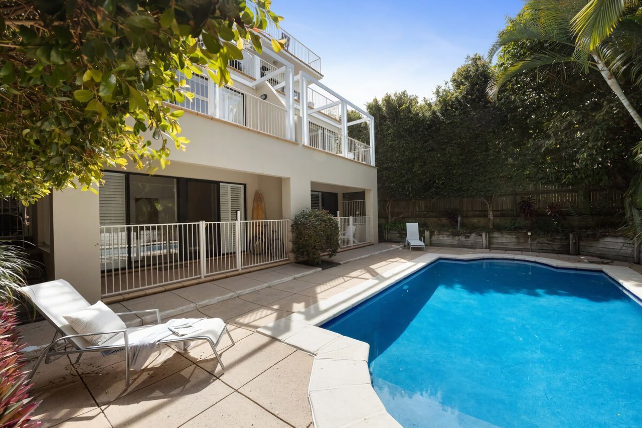 Una casa a due piani con piscina, un balcone e un patio con una poltrona da relax.