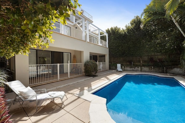 A two-story house with a swimming pool, a balcony, and a patio with a lounge chair.