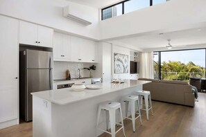 Eine moderne Küche mit weißen Schränken, einem Edelstahlkühlschrank, einer großen Kochinsel mit Hockern und einem Balkon mit Aussicht.