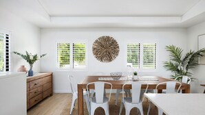 Un comedor con una mesa de madera, sillas blancas, un tapete tejido y un adorno en la pared.